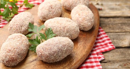 Uncooked meat patties and parsley on wooden table, closeup