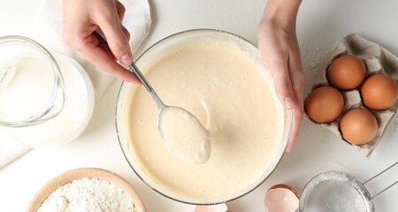 Woman making batter (liquid dough) at white table, top view