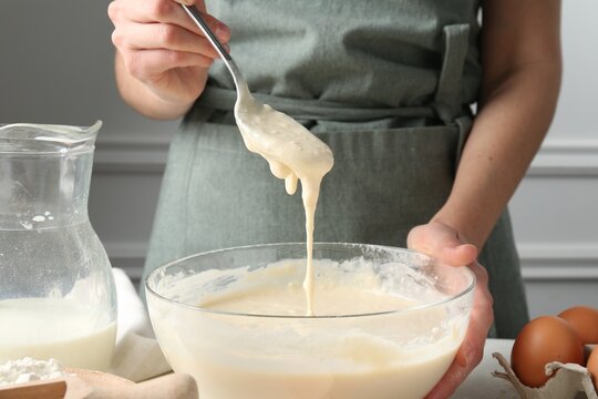 Woman making batter (liquid dough) at white table indoors, closeup