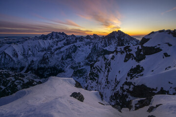 Aerial view of snow-capped peaks pierce the twilight sky, their jagged edges softened by the pastel hues of dawn over Rysy peak, High Tatras, Slovakia.