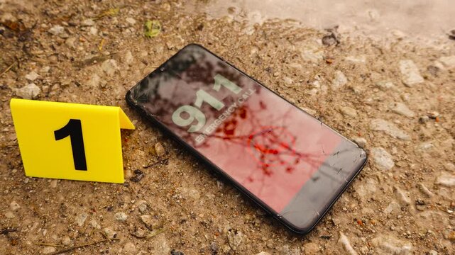 Phone or a smartphone next to a yellow numbered police crime scene marker on brown and golden colored gravel road outdoors with a shiny and reflective puddle or pind next to it. 911 emergency number.