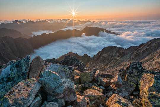 Aerial view of a sun-kissed horizon over the rugged peaks of Maly Ladovy stit piercing through a soft blanket of clouds, Tatranska Javorina, Presov Region, Slovakia.