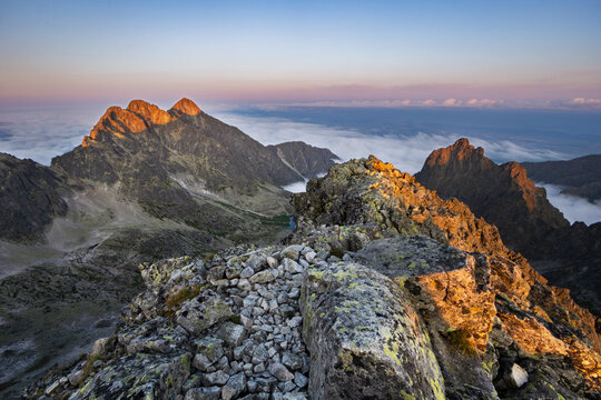 Aerial view of jagged peaks piercing through a soft blanket of clouds, bathed in the warm glow of sunrise around Maly Ladovy stit, Tatranska Javorina, Presov Region, Slovakia.