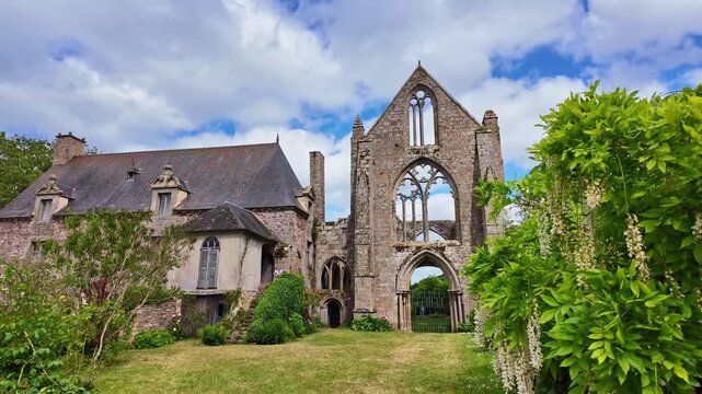 Camera pulls back revealing Beauport Abbey ruins surrounded by flowering trees under a partly cloudy sky.