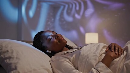 A woman relaxing in bed at night with wireless earbuds. A colorful galaxy projector creates a dreamy atmosphere in the bedroom. Modern wellness and sleep concept