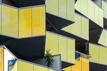 Geometric modern architecture facade featuring yellow balconies and glass panels in minimal structure design with sunlight reflections emphasizing architectural clarity and rhythm.