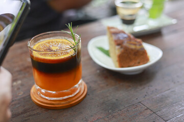 Refreshing glass of iced coffee with orange juice and slice of cake on wooden table at cafe. relaxing moment enjoying fresh beverage and dessert