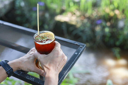 Person hand holding traditional red cup of yerba mate drink, gourd with bombilla. Relaxing outdoor with warm beverage on sunny day in garden