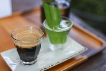 Calm morning beverage set with black coffee and green matcha latte on wooden tray. Refreshing espresso and pandan drink offering moment of relaxation at cafe