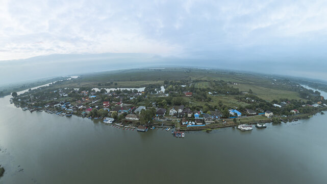 Aerial view of a tranquil community nestled along the riverbank, where homes meet the water's edge, creating a seamless blend of nature and habitation, Bucharest, Romania.