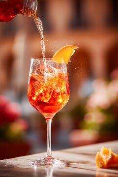Vibrant orange cocktail being poured into a sparkling glass with ice and an orange slice, perfect for summer refreshment and lively celebrations.