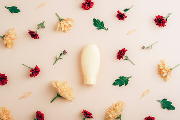 Yellow cosmetic bottle with yellow and red chrysanthemums on beige background. Flat lay, top view, mockup