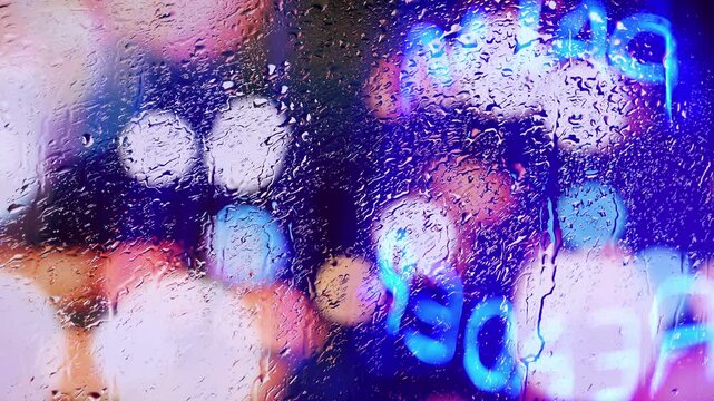Raindrops dripping down a window in an urban city palm reader storefront. Neon lights and colors in the rain downtown.