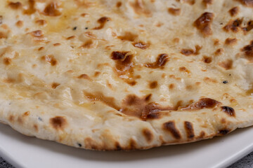 Garlic Naan Bread Traditional Indian flatbread brushed with melted butter and roasted garlic, featuring a soft, chewy texture with golden brown char marks, served on a white plate over a stone texture