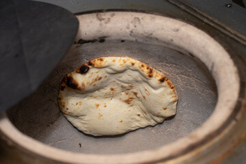 Tandoori Naan Baking Fresh naan bread being cooked inside a traditional clay tandoor oven, showing...