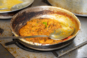 Indian Curry Cooking in Pan Authentic curry preparation on a stovetop, showing a rich, spiced sauce simmering in a metal pan with visible onions and herbs, capturing the texture, colour and aroma