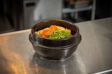 Korean Kimchi Fried Rice Bowl Flavourful Korean-style rice topped with a fried egg, kimchi, sesame seeds, and sliced green onions, served in a traditional black stone bowl on a stainless steel counter