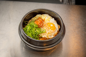 Korean Kimchi Fried Rice Bowl Flavourful Korean-style rice topped with a fried egg, kimchi, sesame seeds, and sliced green onions, served in a traditional black stone bowl on a stainless steel counter