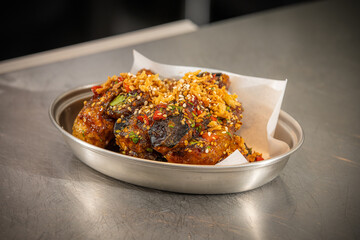 Crispy Asian Chicken Wings – Glazed chicken wings coated in a sticky sweet and spicy sauce, garnished with sesame seeds, fried onions, and chopped chili, served in a metal dish