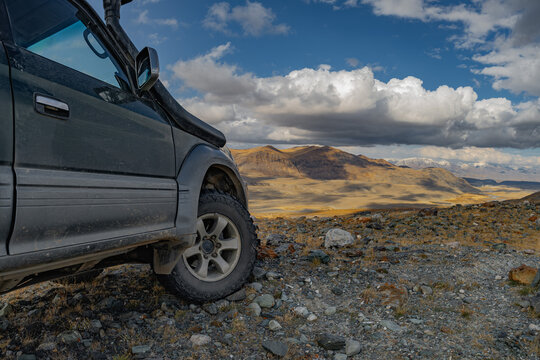 An off-road vehicle with mud tires is parked on rocks overlooking the mountains. Off-road tires on rocks overlooking the mountains and the blue sky. A car tire against the backdrop of the mountains.