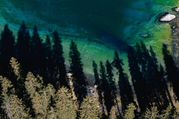 Aerial view of the mesmerizing Lago di Carezza's turquoise waters meet the dark shadows of the surrounding dense evergreen forest, Karersee, Trentino-Alto Adige, Italy.