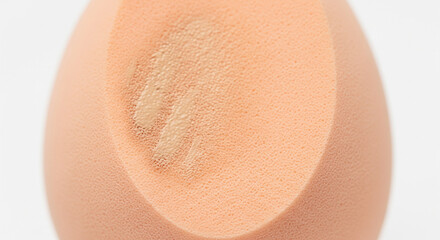 Fototapeta premium Makeup Sponge with Applied Foundation Swatch for Product Testing. Extreme close-up shot of a peach- or nude-colored makeup blending sponge, prominently featuring a visible swipe