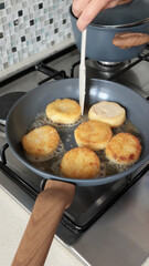 Anonymous person fries potato croquettes in vegetable oil in new, trendy frying pan. Farm produce. Home cooking. Traditional cuisine.