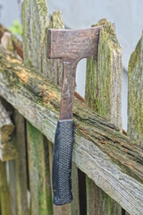 one big axe with gray black handle lies on grey wooden board of fence on rural street