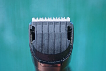 Part of one black electric hair clipper with gray metal blades and teeth on a green background