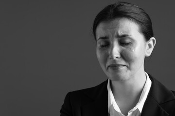 Businesswoman in suit crying on grey background, space for text. Black and white effect