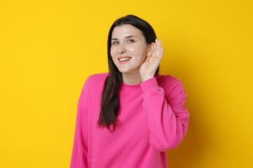Fototapeta premium Smiling woman showing hand to ear gesture on yellow background