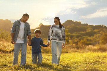 Happy family holding hands in field at sunset. Space for text