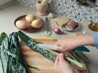 Anonymous person peels kale with knife, removing tough part, on wooden board at home. Healthy eating, farm-grown produce.