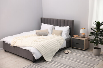 Fototapeta premium Large bed with linens, nightstand and houseplant near grey wall in bedroom. Interior design