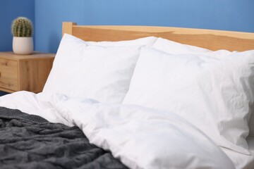 Bed with cozy fresh linens near blue wall indoors, closeup