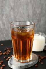 Tasty iced coffee, milk and beans on black wooden table