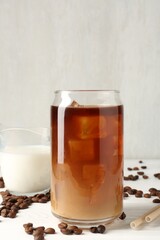 Tasty iced coffee with milk and beans on white wooden table