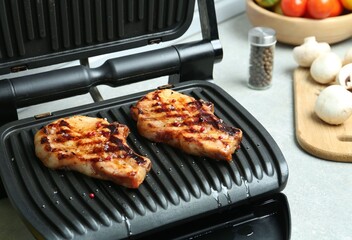 Electric grill with delicious steaks on light table in kitchen, closeup