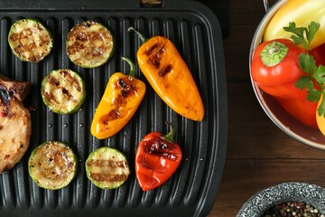 Electric grill with steak and vegetables on wooden table in kitchen, flat lay