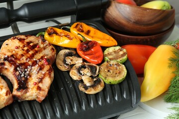 Electric grill with delicious vegetables and steaks on white wooden table, closeup