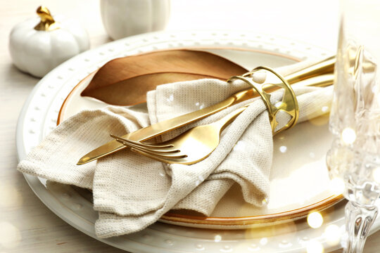 Autumn place setting, bokeh lights. Plates, cutlery and fall decor on table, closeup