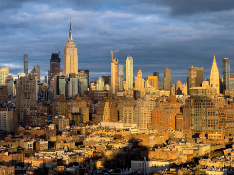 View of towering skyscrapers bathed in golden sunlight pierce through the cloudy sky, creating a stunning contrast of light and shadow, New York, New York, United States.