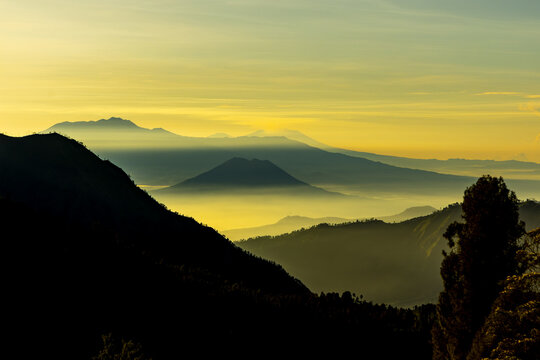 View of a majestic mountainscape shrouded in ethereal mist, where golden light kisses the peaks, painting a serene panorama, Bromo, East Java, Indonesia.