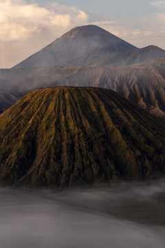 View of the rugged volcanic landscape, where the peaks rise above a blanket of mist, creating a dramatic contrast of light and shadow, Bromo, East Java, Indonesia.