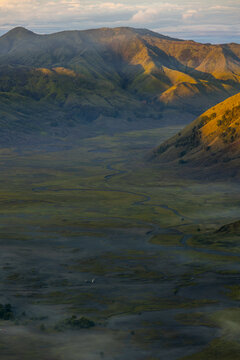 View of golden sunlight kissing the rugged mountain peaks as mist hangs low over the vast, grassy plains creating a serene landscape, bromo, East Java, Indonesia.