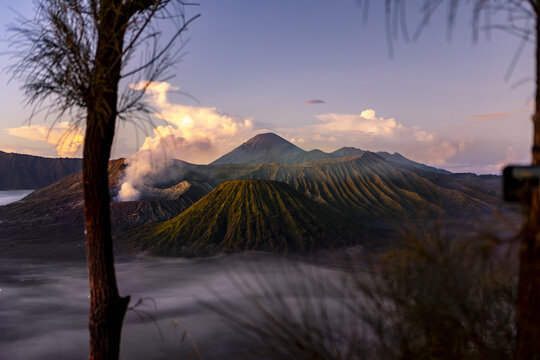 View of a majestic volcano rises above a sea of mist, its slopes catching the warm glow of the setting sun, creating a stunning contrast of light and shadow, Bromo, East Java, Indonesia.