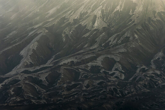 View of rugged, textured mountains under a hazy sky, with stark contrasts of light and shadow creating a dramatic, otherworldly landscape, Bromo, East Java, Indonesia.