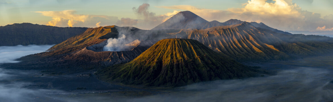 View of the volcanic landscape where golden light paints the textured slopes and smoke rises gently from the crater, Bromo, East Java, Indonesia.