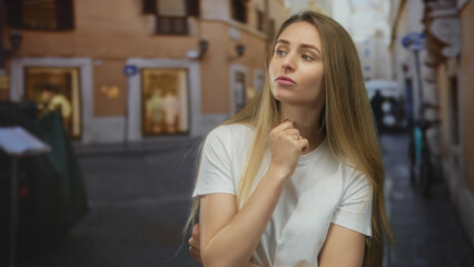 Woman pondering on a city street with long hair in a casual setting, exuding a thoughtful mood and casual fashion against a blurred urban backdrop in the background.