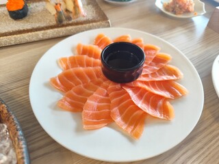 Thinly sliced ​​salmon served on a white tile tray with soy sauce in a small black cup.
